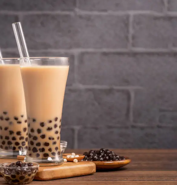 Photo of Delicious bubble milk tea with straw in drinking glass on wooden table background, concept of reduce plastic to go in Taiwan, close up, copy space