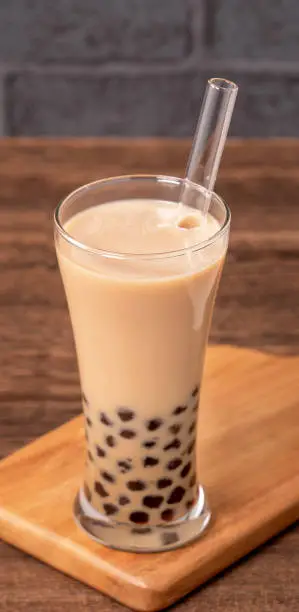 Photo of Delicious bubble milk tea with straw in drinking glass on wooden table background, concept of reduce plastic to go in Taiwan, close up, copy space