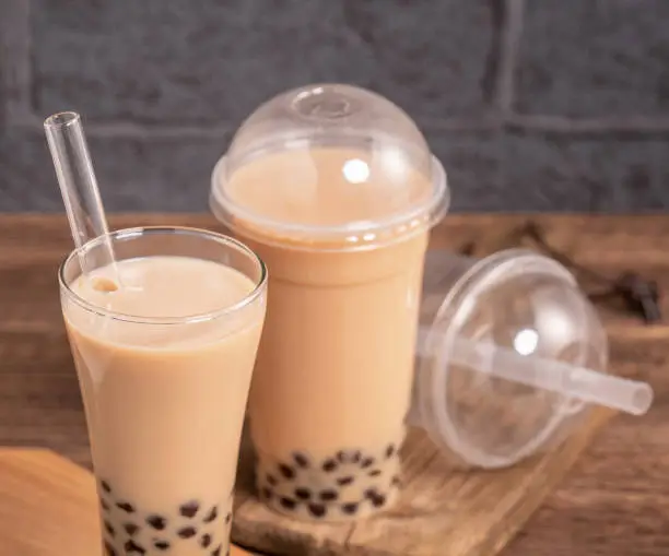 Photo of Delicious bubble milk tea with straw in drinking glass on wooden table background, concept of reduce plastic to go in Taiwan, close up, copy space