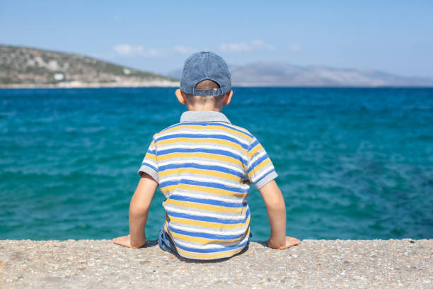 istock Boy sit on pier back and look to sea. 1154393400