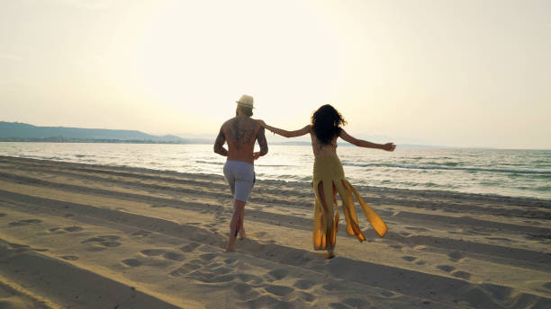 Young couple walking on the beach Young couple walking on the beach. body adornment rear view young men men stock pictures, royalty-free photos & images