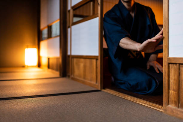 Traditional japanese house or ryokan with man in kimono opening shoji sliding paper doors sitting on tatami mat floor Traditional japanese house or ryokan with man in kimono opening shoji sliding paper doors sitting on tatami mat floor yukata photos stock pictures, royalty-free photos & images
