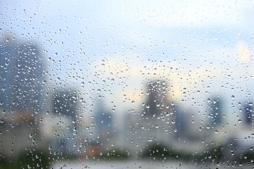 office window covered with rain water. water spray on window. after rain traffic, worker stuck in the office concepts. blur urban skyline background. rainy season concepts.