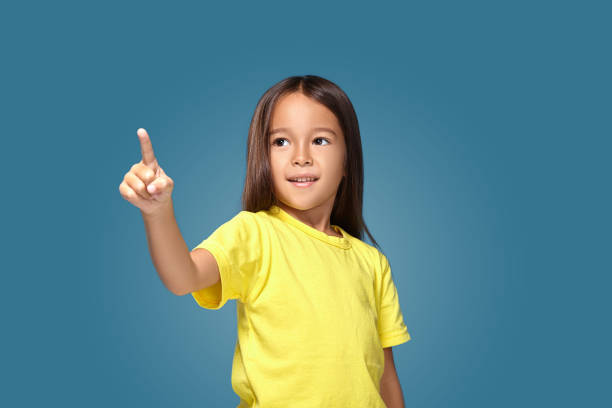 istock Cute girl shows finger on blue background 1154405424