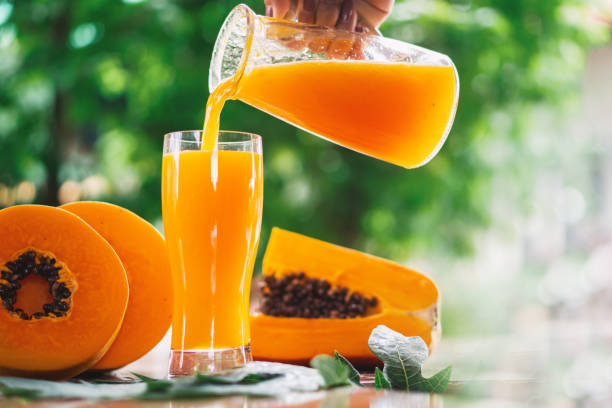 donna mano versando succo di papaia su bicchieri con fetta di papaia su sfondo di legno - papaya foto e immagini stock