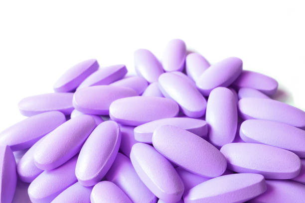 pila di pillole di integratore di colore viola lilla di forma ovale su sfondo bianco - pill purple capsule vitamin pill foto e immagini stock