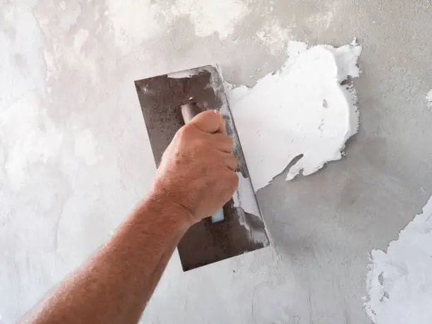 Photo of Builder using plastering tool for finishing old wall.