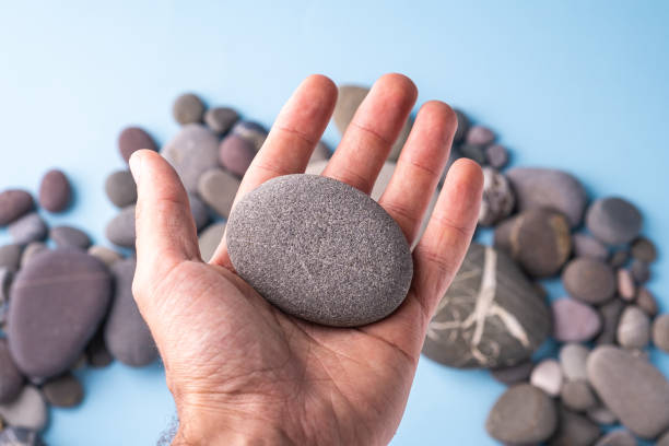 istock Pebble stone hold in hand on blue background with pebbles 1154413412