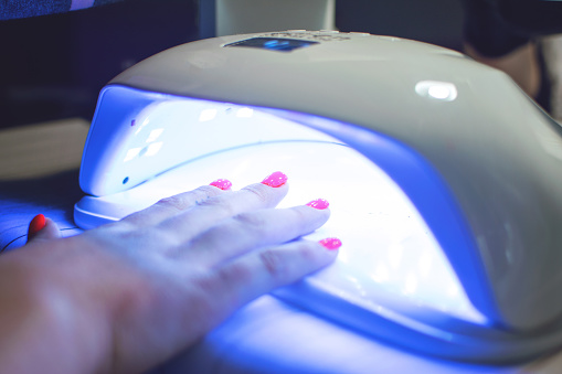Female Hand with red nails in the lamp for manicure. Nail Lamp Dryer for Gel Nail Polish Curing Manicure Pedicure.