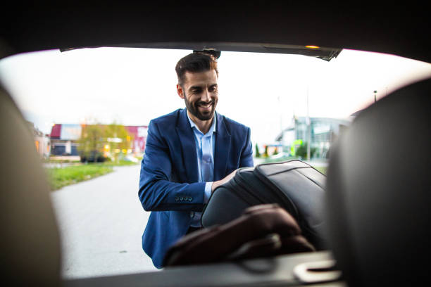 Young Handsome businessman packing bag in car trunk for business travel, smiling