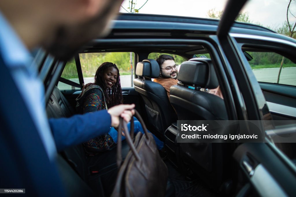 Man entering ride sharing car Young, handsome man entering a car, holding luggage, his friends sitting in car and waiting for him Car Pooling Stock Photo