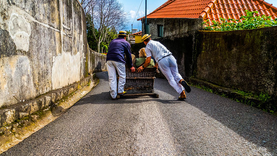 Monte, Madeira, March 18, 2017, Basket sled with tourists inside powered by two carreiros racing down the narrow street from monte to funchal