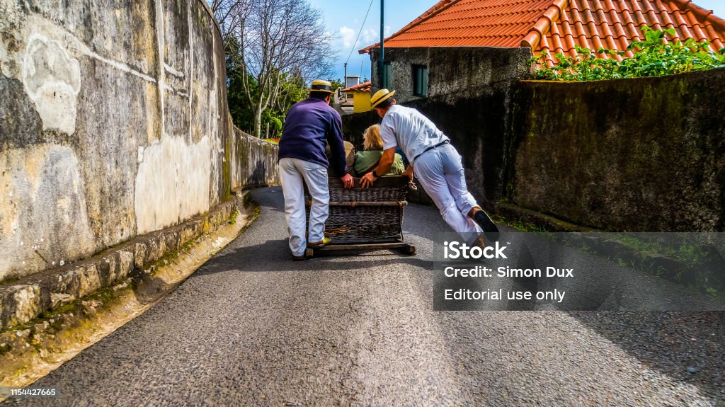 Monte, Madeira, March 18, 2017, Basket sled with tourists inside powered by two carreiros racing down the narrow street from monte to funchal Sled Stock Photo