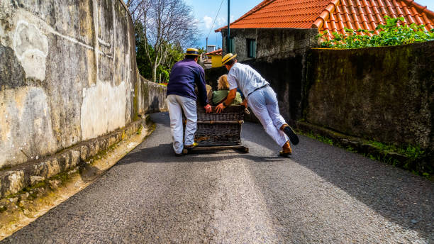 Monte, Madeira, March 18, 2017, Basket sled with tourists inside powered by two carreiros racing down the narrow street from monte to funchal stock photo