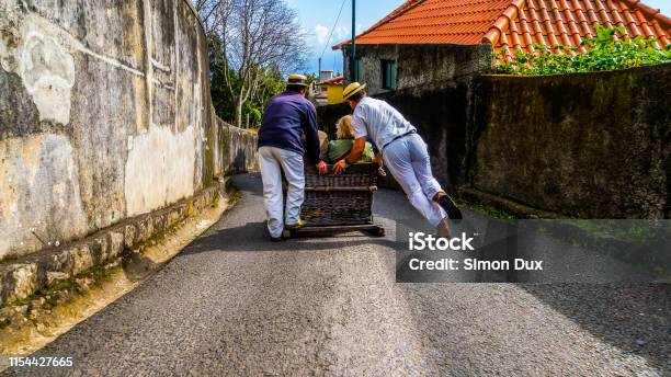 Monte Madeira March 18 2017 Basket Sled With Tourists Inside Powered By Two Carreiros Racing Down The Narrow Street From Monte To Funchal Stock Photo - Download Image Now