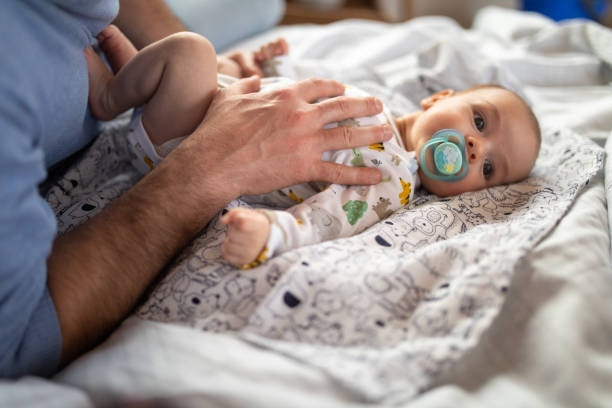 istock Baby with pacifier lying on bed with unrecognizable dad 1154430649