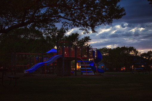 An empty playground with equipment under a cloudy sky in a nighttime landscape