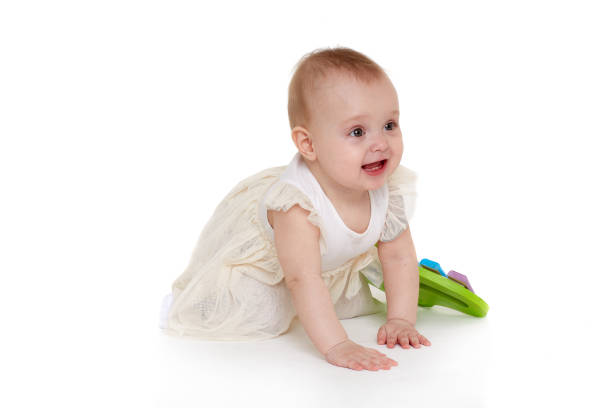 Close up portrait of an adorable one years old baby girl smiling, sitting on the bed in her nursery room,  playing with wooden rattle toy.