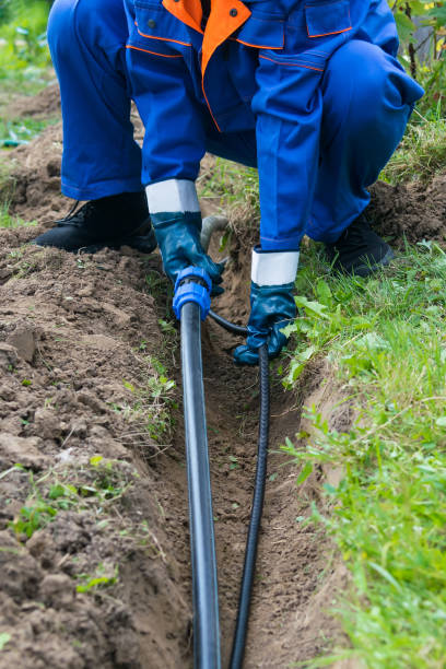 istock a man in special clothes puts a long black pipe for the water supply 1154448974