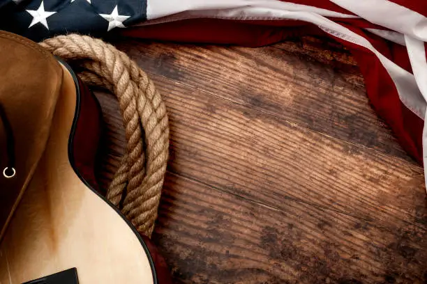 Photo of American culture, living on a ranch and country music concept theme with a cowboy hat, USA flag, rope lasso and acoustic guitar on a wooden background in a old saloon with copyspace