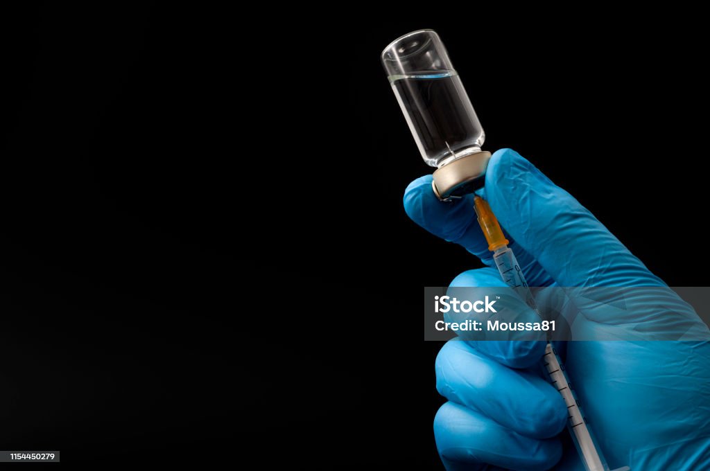 Insulin shot, flu jab or medical injection concept theme with doctor or nurse hands wearing blue surgical latex gloves filling a syringe from a glass vial isolated on black background with copyspace Insulin shot, flu jab or medical injection concept theme with doctor or nurse hands wearing blue surgical latex gloves filling a syringe from a glass vial isolated on black background with copy space Syringe Stock Photo