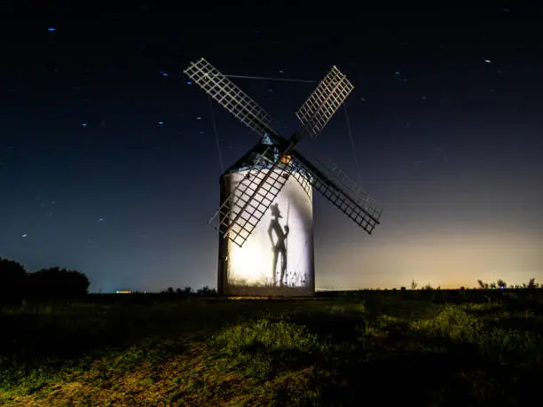 Night photograph of a windmill with the silhouette of don Xijote making a shadow.