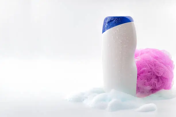 Photo of Personal hygiene and body care toiletries concept theme with a bottle of shower gel soaked in water drops, bubbles made by soap foam and pink shower sponge isolated on white background with copyspace