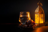 Muslim religious tradition, holy month of Ramadan, Islam and Iftar concept theme with a bowl of dates, prayer beads, glass of water and Arabic lantern on black background with copyspace
