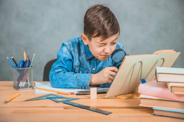istock Inquisitive little boy is looking through magnifying glass at something in his book like detective. 1154456089