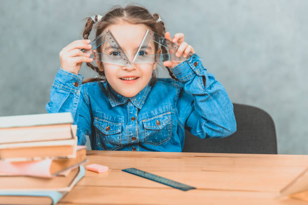 istock Funny little inquisitive girl playing around during the learning process, looking through two triangle. 1154456253