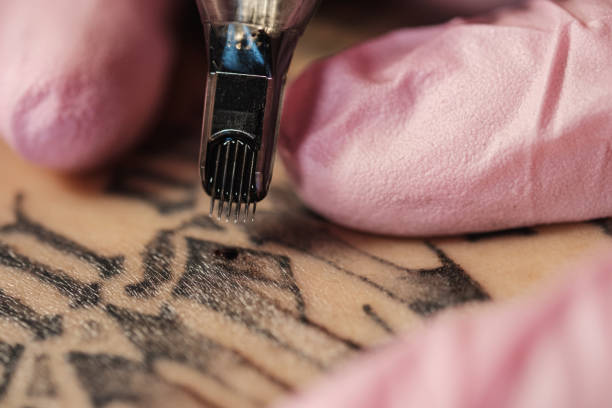 primer plano de una aguja de tatuaje. el proceso del maestro del tatuaje. guantes de protección de mujer rosa. - tattoo machine fotografías e imágenes de stock