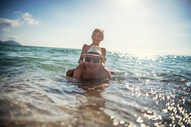 Little boy playing with his grandfather in the sea. The boy is riding grandfather and is laughing.\nNikon D850