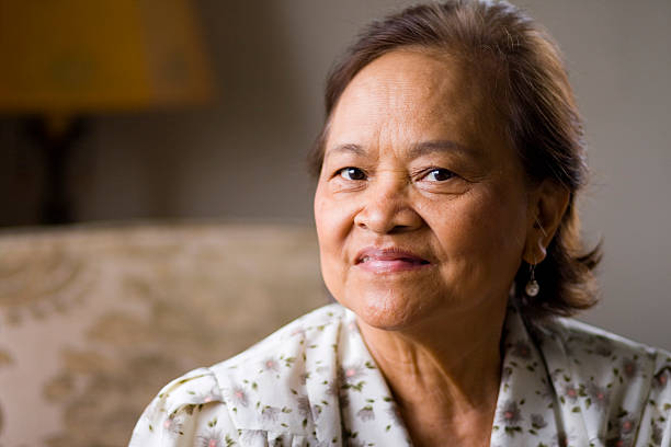 istock Smiling senior Asian woman sitting on a sofa 115447789
