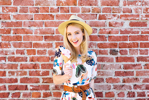 Beautiful smiling young woman stands by a brick wall with an ice cream in her hand in the summer