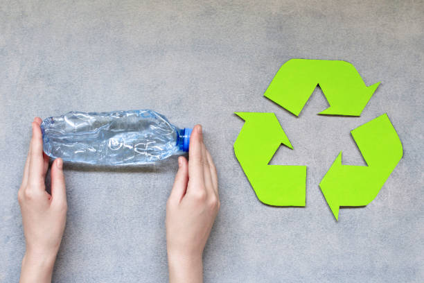 istock Woman hands holding plastic bottle with recycle symbol on grey background. 1154485998