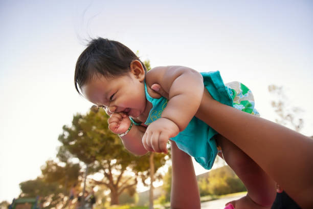 Baby girl being lifted up by mother into the sky, baby looks excited and nervous. stock photo