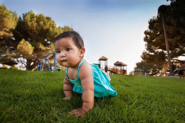A curious little baby girl crawls away from a kids playground to explore, and is unsupervised by parents. stock photo