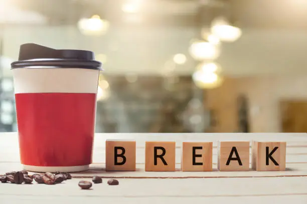 Photo of Coffee break concept. Paper coffee cup and wood letter with blurred coffee shop background.