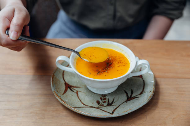 istock Hand scooping Classic Pureed Pumpkin Soup topping with pepper. Served in ceramic cup on wooden table. 1154517536