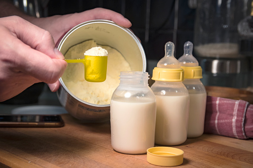 Hand holding scoop of powdered baby formula, ready to mix in bottles