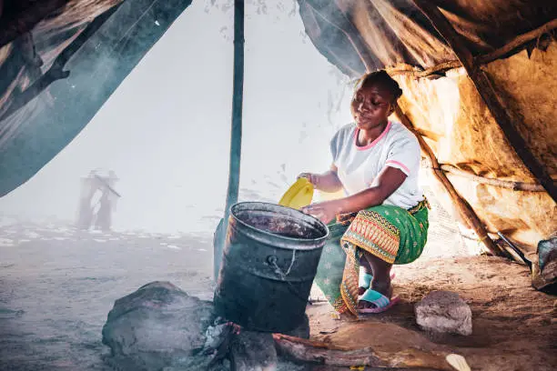 Africa, Village Life, Routines - A Young African Woman Boiling Water in a Tin Container inside a Hut
