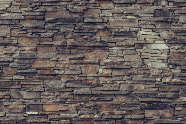 Brown brick wall. Stone weathered backdrop, granite facade surface, rock textured. Decorative dirty tiles on the wall. Grunge urban background. Old stony texture for decoration