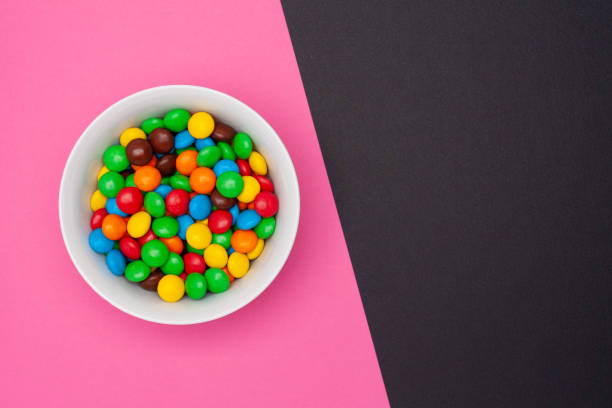 istock White bowl with chocolate round colored candies on a pink background with copy space. Top view. 1154537488