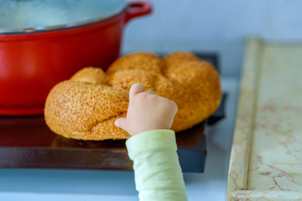The hand of a hungry child hold and break a piece of bread. The hand of a hungry child hold and break a piece of bread. A kid's hand tearing a piece of challah. Hot plate for the Sabbath. Pot with traditional food and challah-special bread in Jewish cuisine. jewish sabbath photos stock pictures, royalty-free photos & images