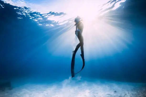 Freediver girl in bikini over sandy sea with fins.