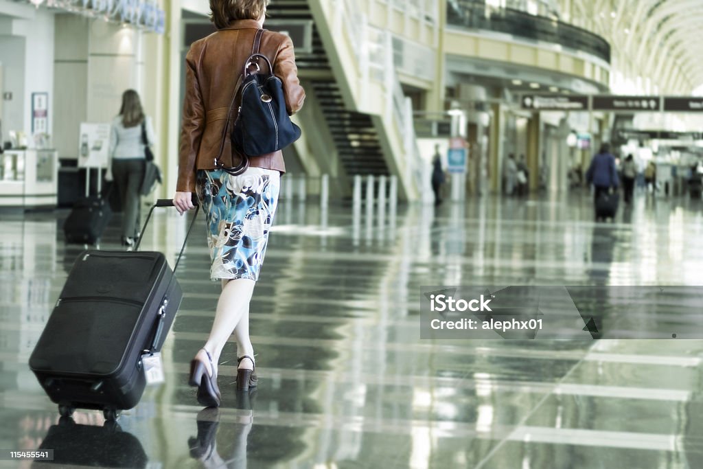 A woman carrying her suitcase in an airport Woman toting luggage for a trip. Leaving Stock Photo