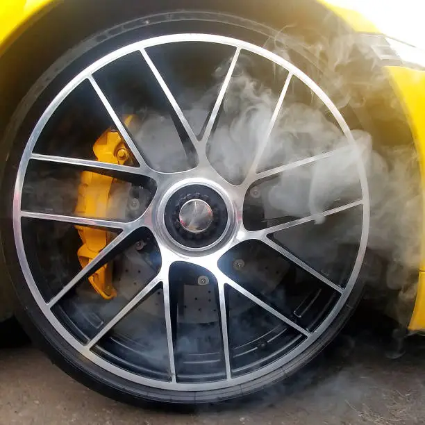 Photo of Yellow car with light alloy wheels with carbon ceramic brakes and smoke from it. Close up, square image