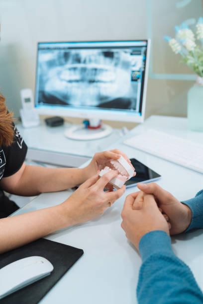 zahnärztin hält zahnform und erklärt ihrer patientin während der ärztlichen beratung in ihrer klinik etwas. kieferorthopädin zeigt ihre mandantin prothese. erfahrung, medizinisches behandlungskonzept. - laboratory dentures dental hygiene human teeth stock-fotos und bilder