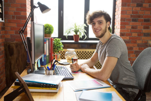 istock Young smiling man working at his workplace sitting over window holding marker 1154561670