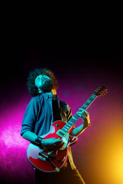 giovane hipster con i capelli ricci con chitarra rossa in luci al neon. il musicista rock suona la chitarra elettrica. - guitarist foto e immagini stock